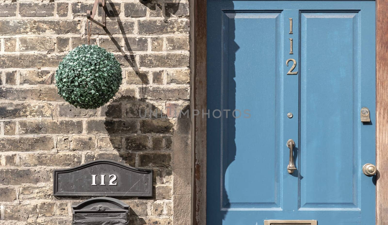 London, UK - May 08, 2025 - Blue composite door is closed with Door knocker, Letter box and Artificial topiary ball decoration on Brick wall front of the House number 112. use it as your Wallpaper, Poster and Space for text, Selective focus.