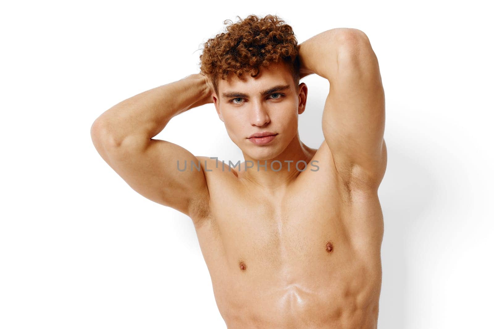 Athletic young man displaying a strong physique and charisma, with curly hair and a confident expression. Minimalist white backdrop emphasizes his features.