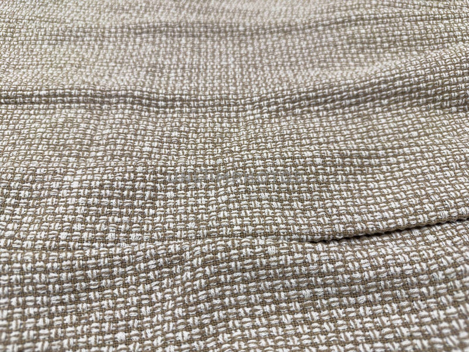 A close-up view of a woven fabric featuring a subtle pattern in soft beige and cream. The material has a textured surface, ideal for crafting and upholstery at home.