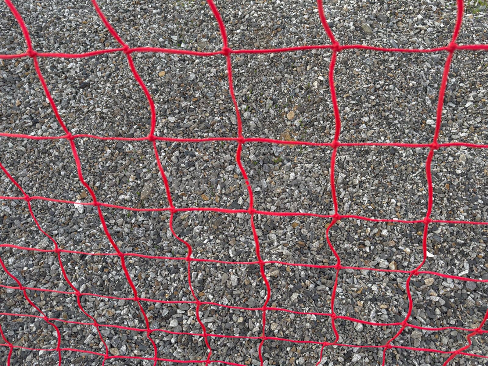 A red mesh fence surrounds a construction site, securing gravel and preventing access. The vibrant color contrasts with the gray gravel, creating a noticeable barrier.