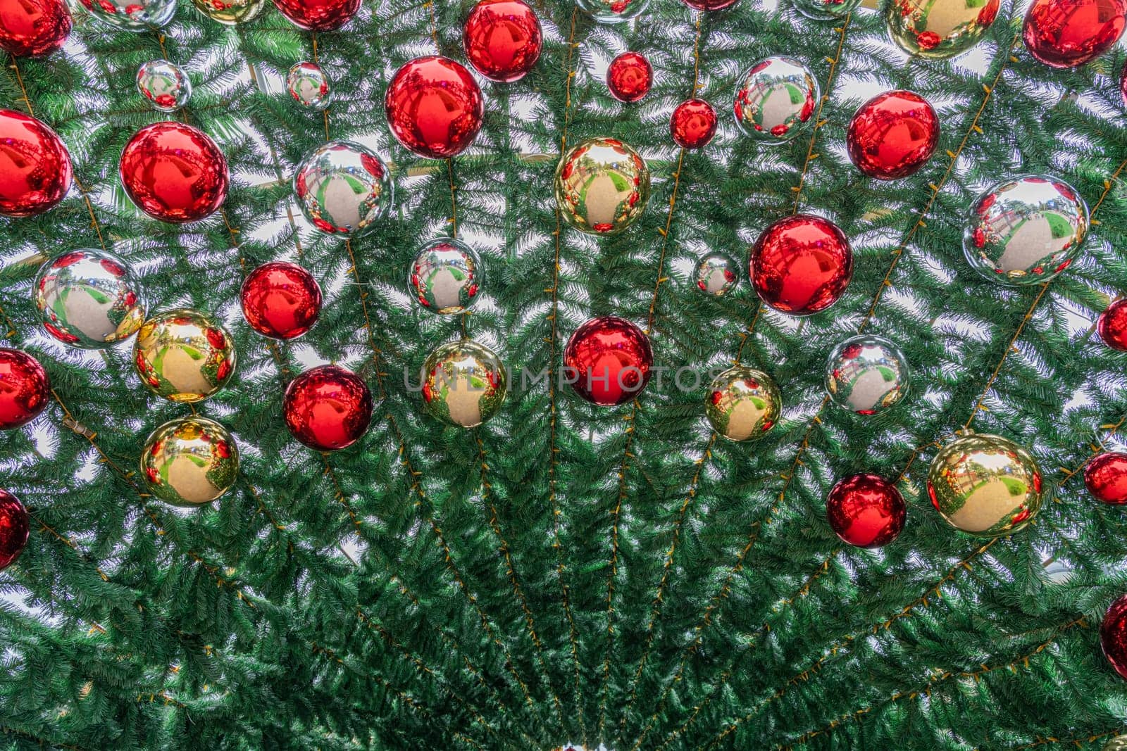 Bright red and gold ornaments adorn an evergreen tree, creating a festive atmosphere. The circular decorations reflect light, enhancing the holiday spirit during winter celebrations.