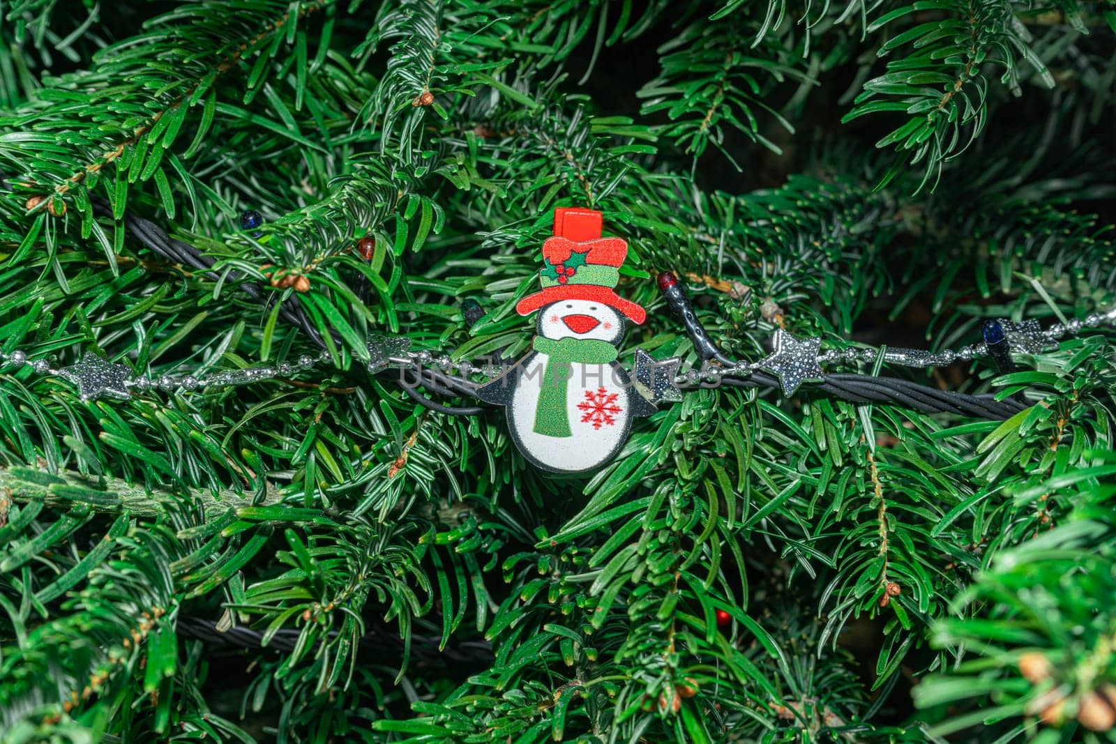 A vibrant Christmas tree adorned with a cheerful snowman ornament, sparkling lights, and lush green branches, evoking a festive atmosphere during the holiday season.