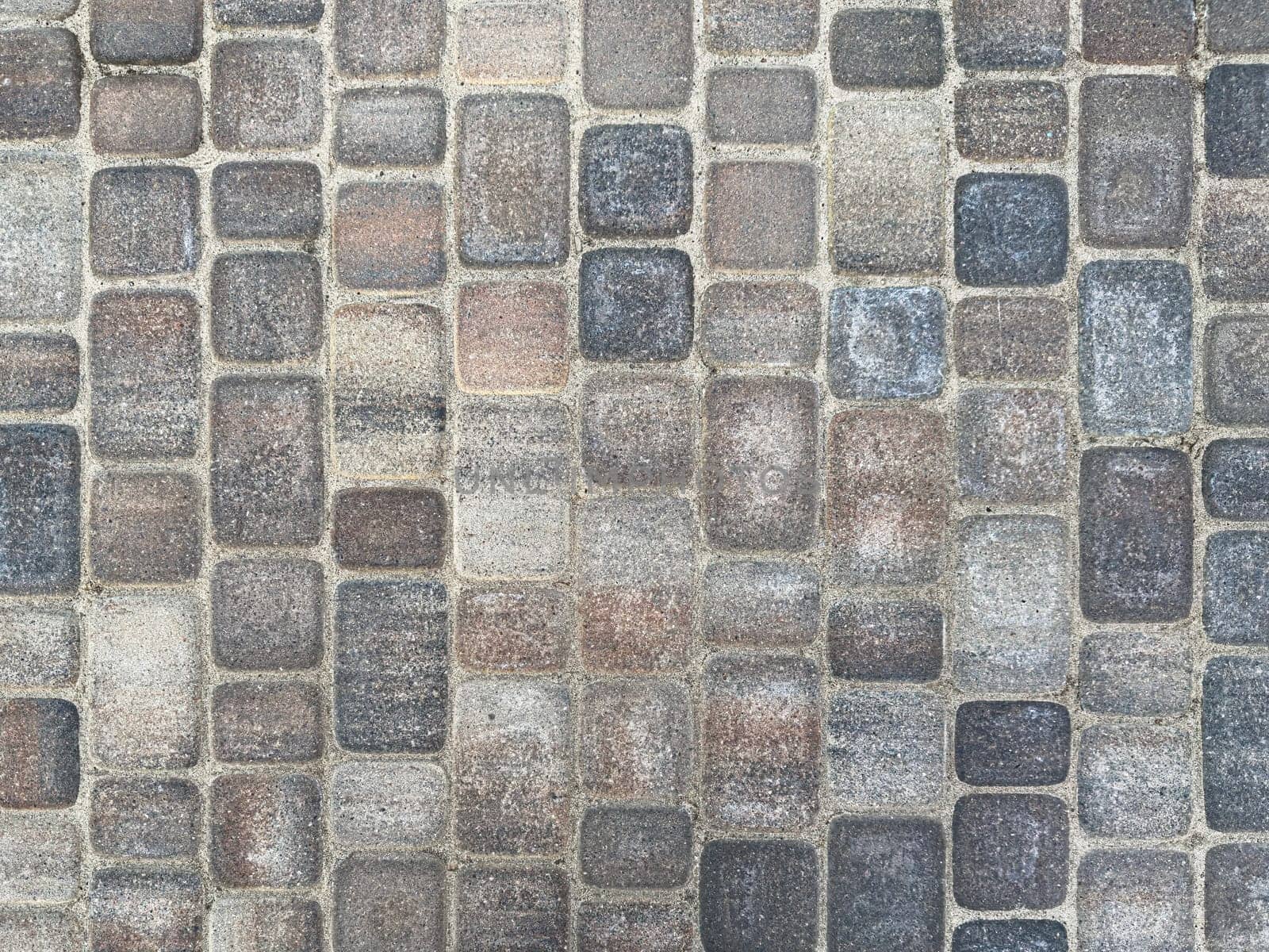 A close-up view of a cobblestone walkway showcases various shades of gray and brown stones arranged in a structured layout. This urban setting highlights the craftsmanship of stonework.