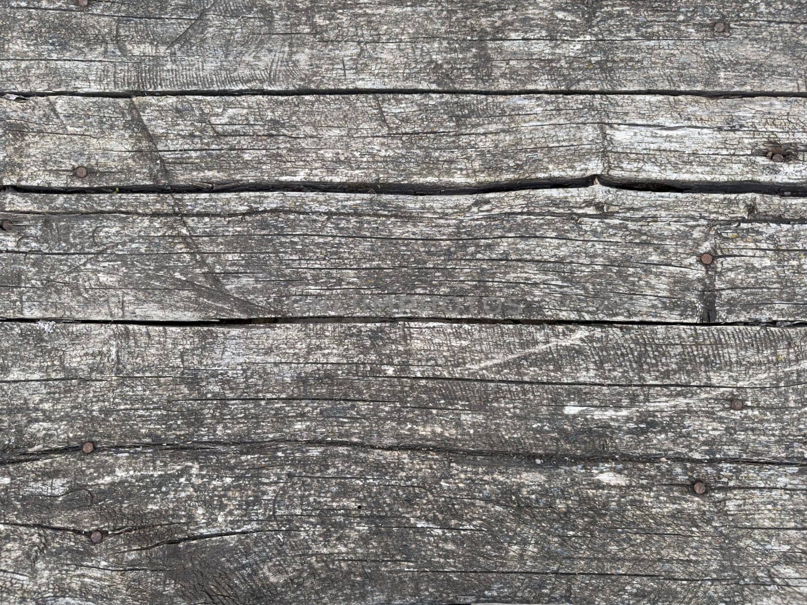 The surface features old, weathered wooden planks with a varied texture and gray tones. The natural aging enhances the rustic charm of the outdoor setting, inviting relaxation.