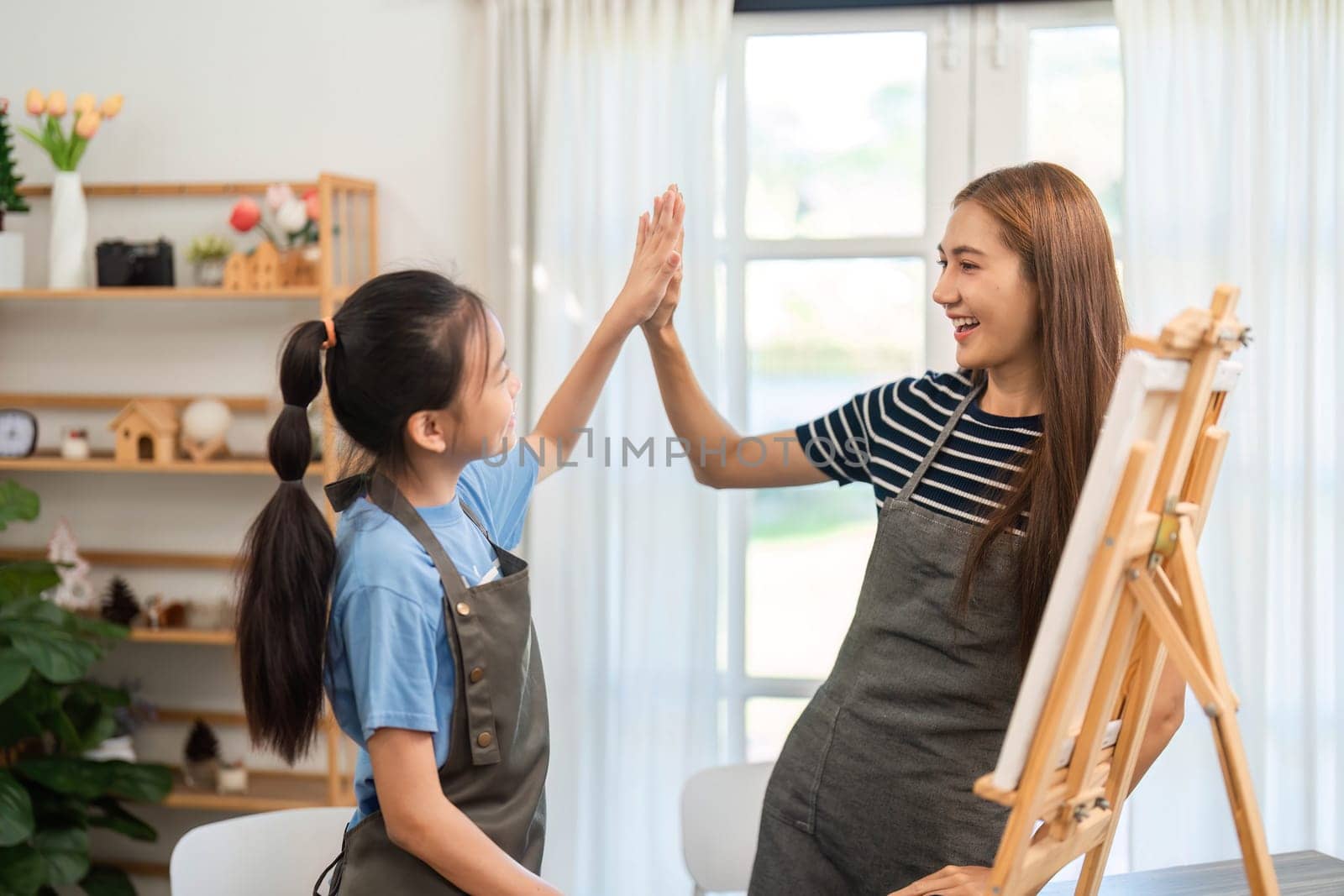 A proud mother and daughter high-fiving each other during a fun art session, celebrating creativity and teamwork in a cozy setting.