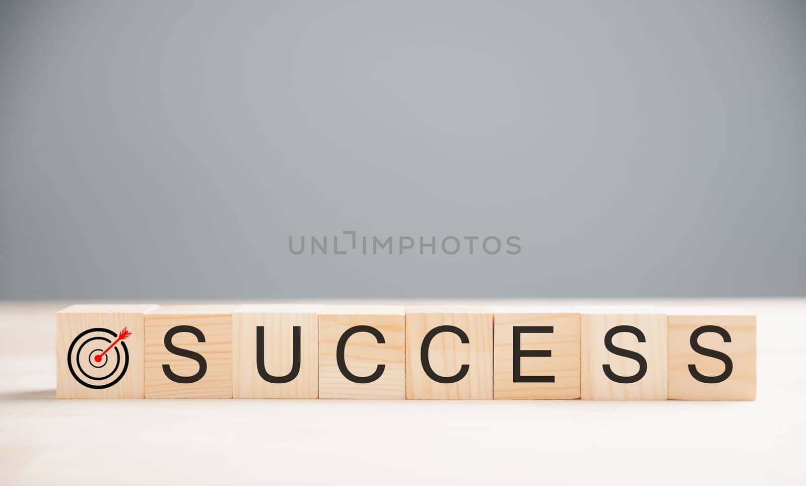Wooden cube placed over the word success on a wood table, highlighting the target success concept. Captured on a grey background with ample copy space.