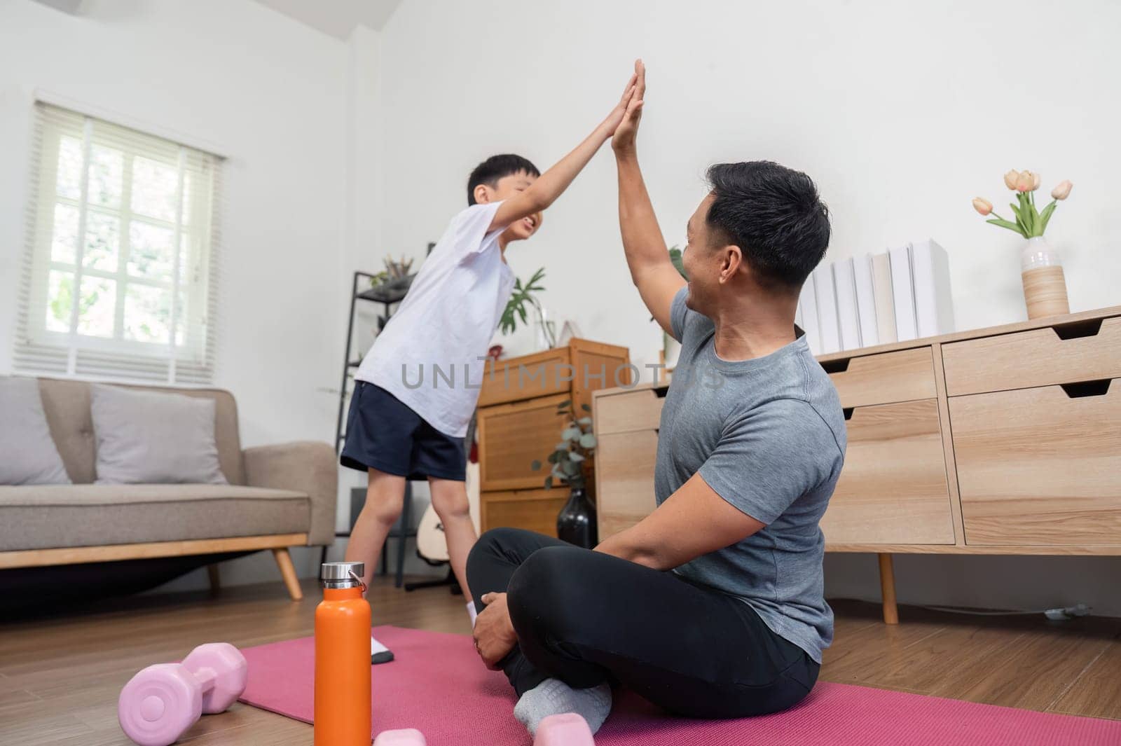 A joyful moment captured of a father and son high-fiving during a fun fitness session at home, celebrating their bond and activity.