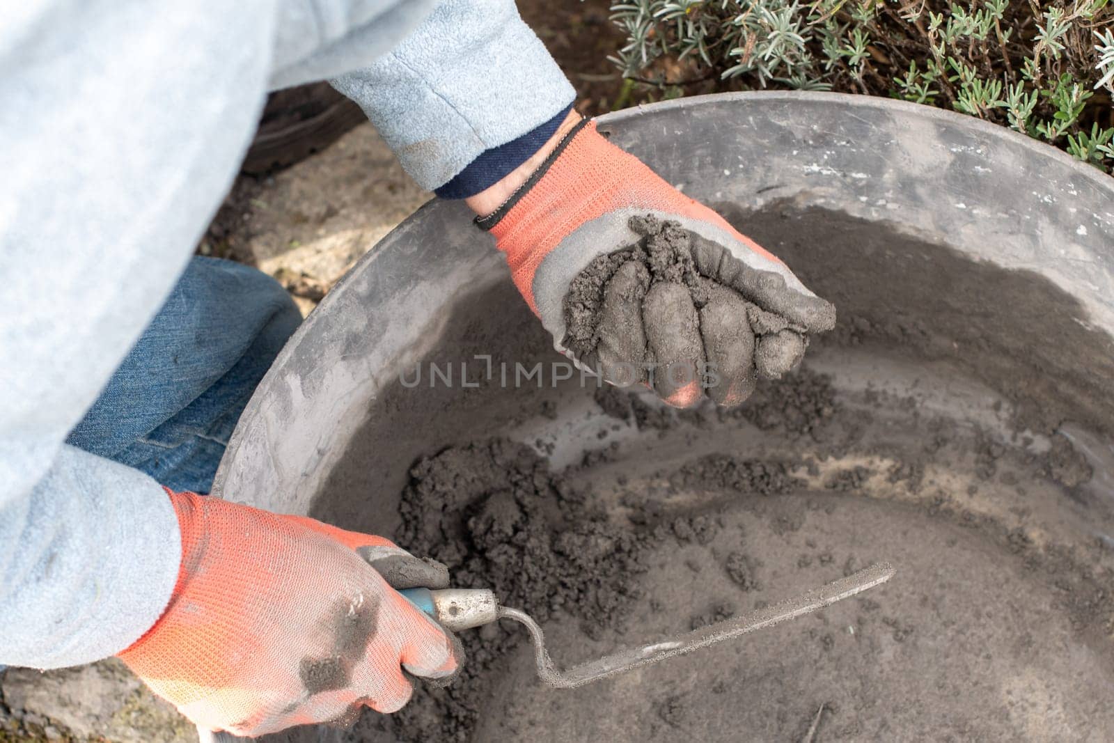 Construction worker wearing gloves mixes cement mortar in a bricklaying basin, ensuring the optimum texture for a strong bond