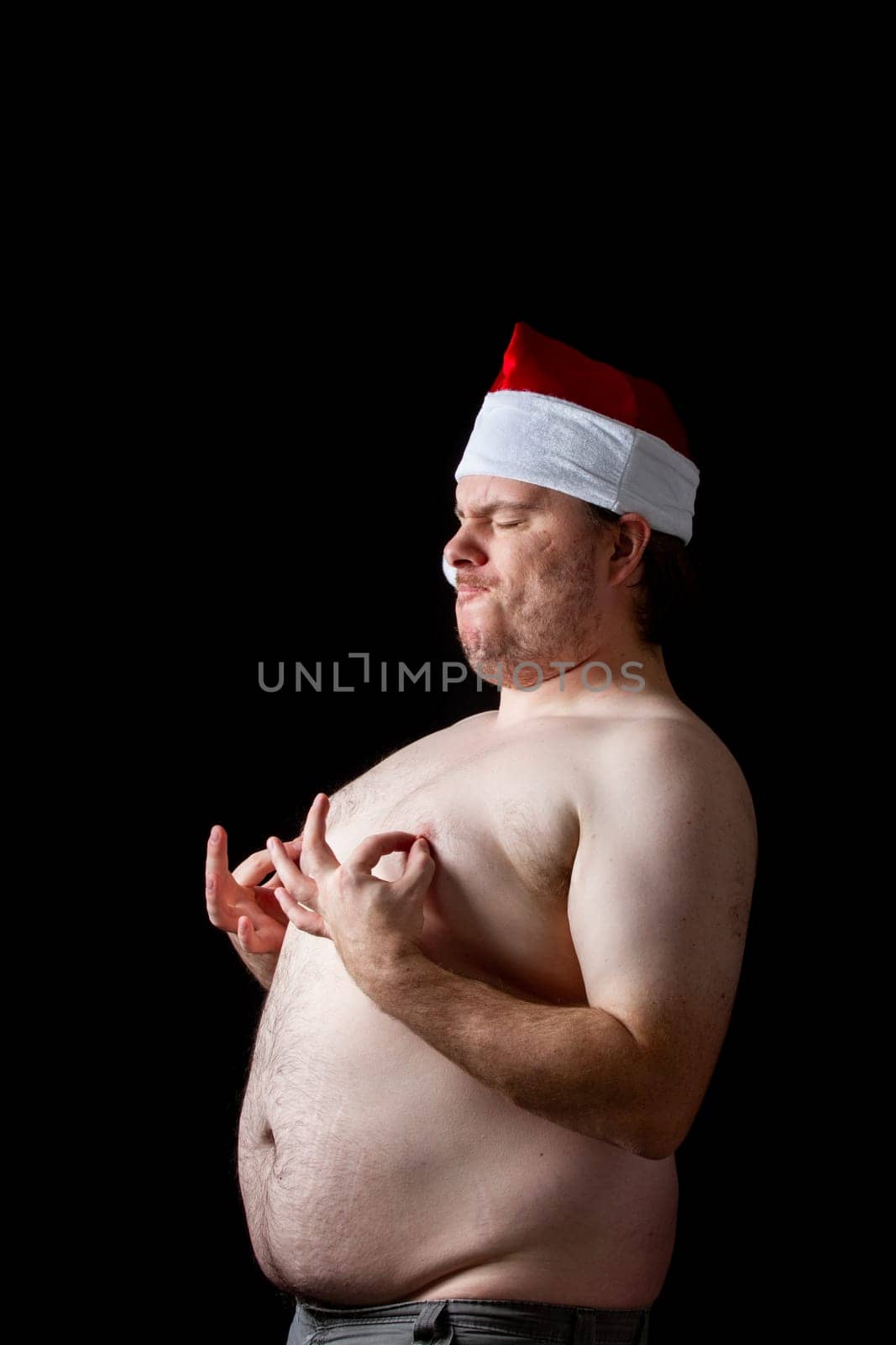 A man is standing in a black background with his hands on his chest and a red hat on his head