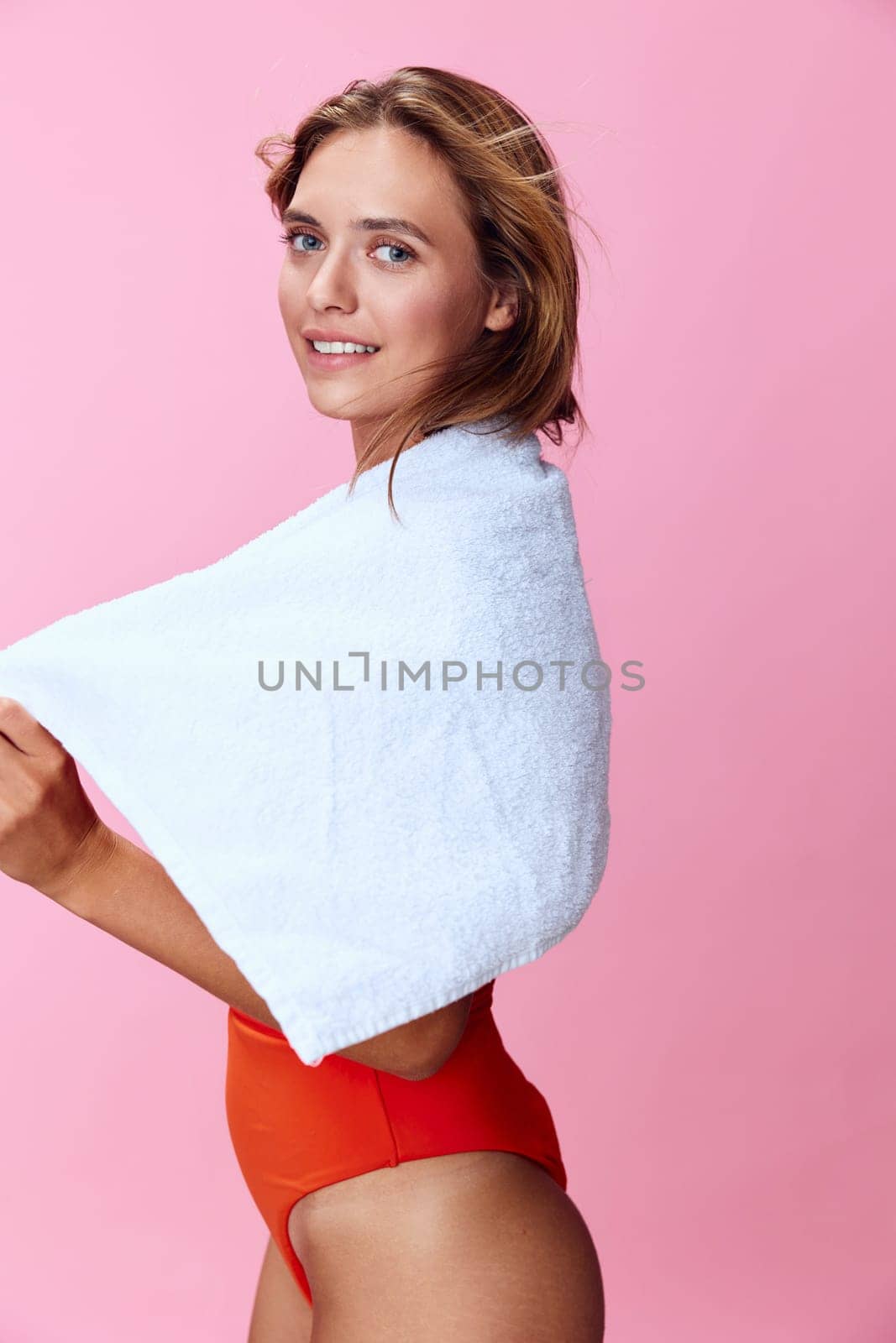 Vibrant summer fashion a stylish woman in an orange swimsuit and white towel posing against a pink background