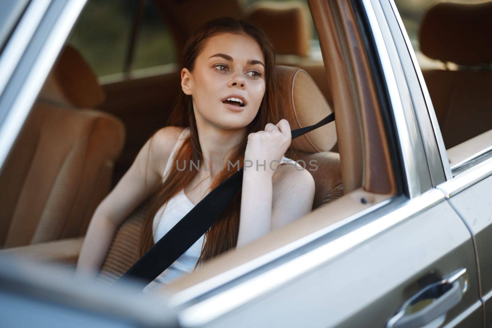 A young woman in a casual outfit sitting in a car during a road trip, smiling while looking outside, conveying emotions of freedom and adventure, perfect for travel-themed projects.