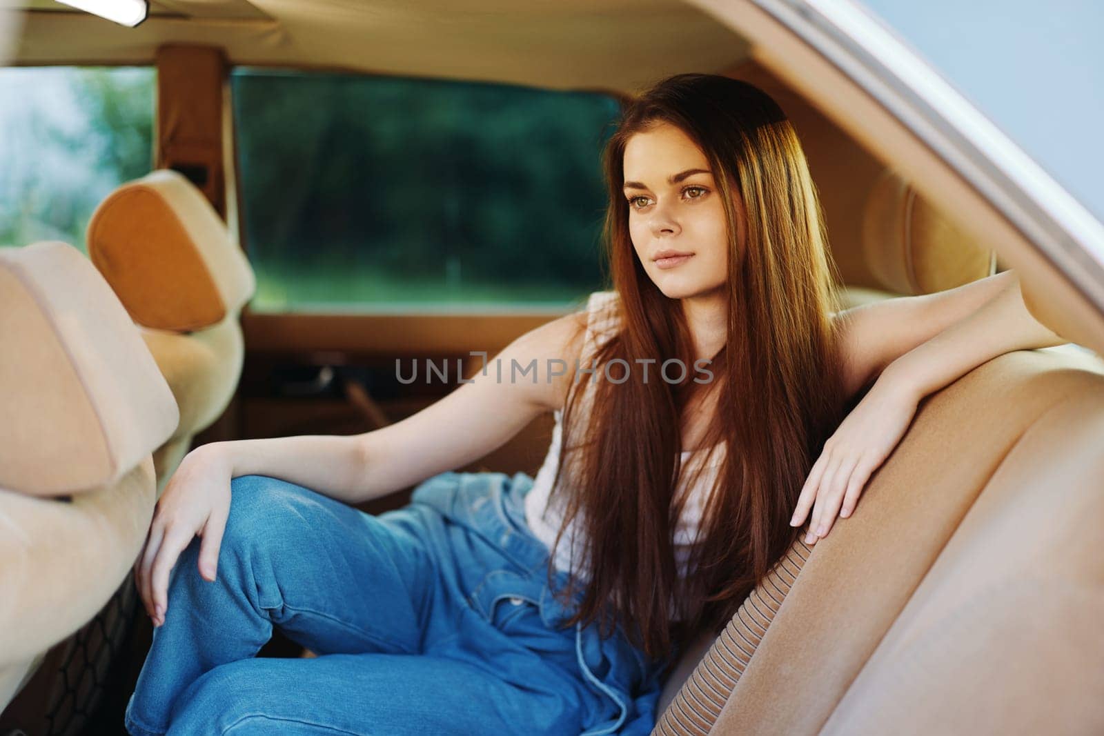 A young woman in denim and a light top sits casually in a classic car, exuding a relaxed summer vibe with her long hair and contemplative look, perfect for lifestyle themes.