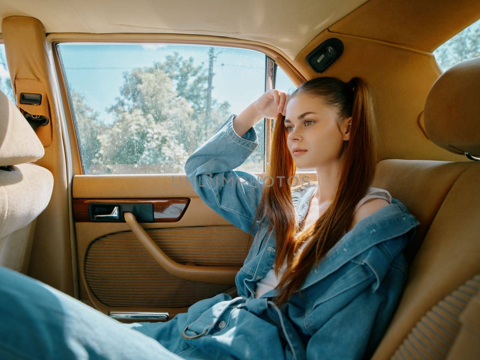 Pensive young woman in casual denim attire, sitting in a vintage car, reflecting on life. Bright daylight enhances the mood, perfect for lifestyle and fashion themes.
