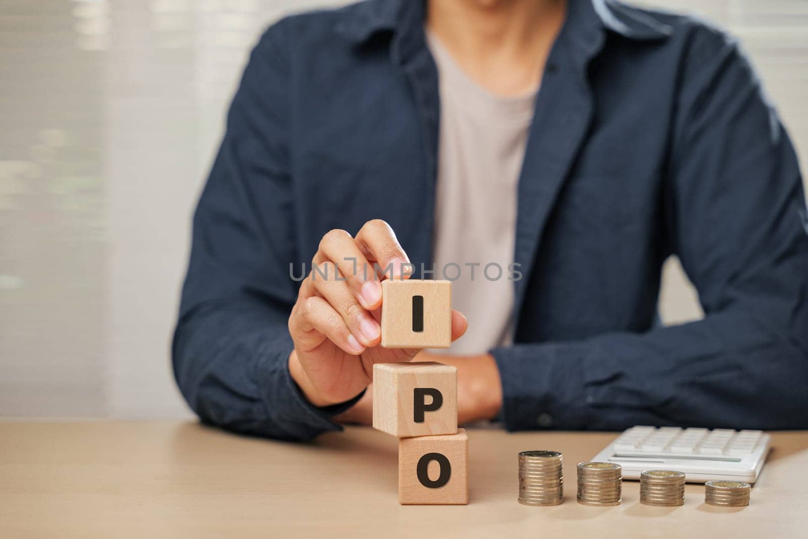 Close up businessman hand holding wooden cube blocks spelling IPO near coins and a calculator. Represents Initial Public Offering, planning, employee initiatives, and business financial accountability