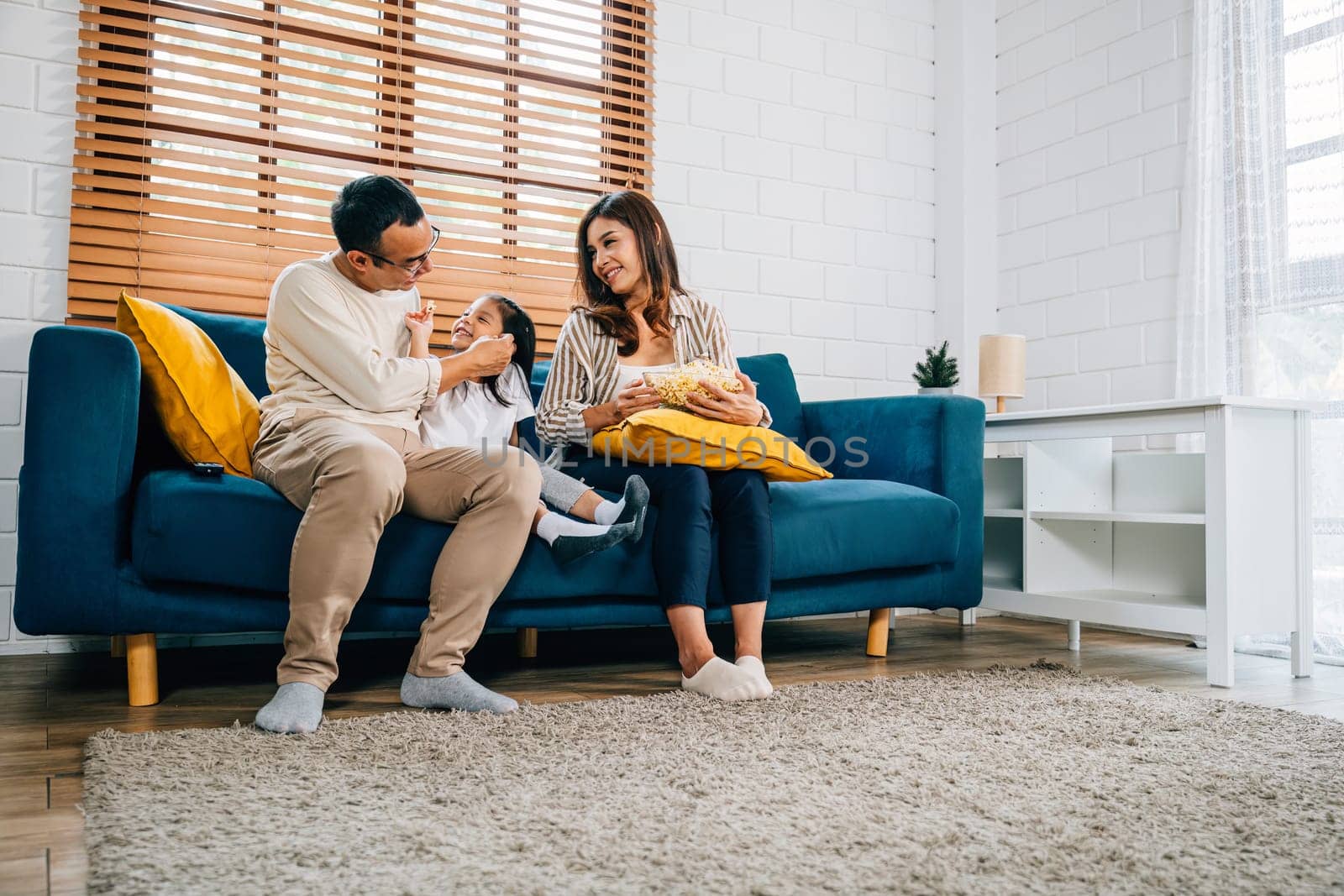 In their warm home family finds joy in watching TV and sharing popcorn. father mother daughter and sibling are all smiles creating an atmosphere of togetherness and happiness.
