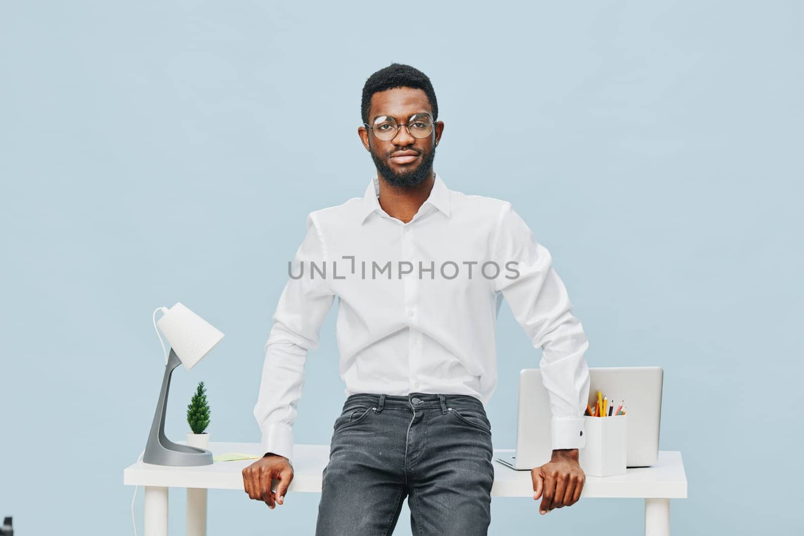 Happy young man with glasses and well-groomed appearance in casual white shirt standing at a clean desk with office supplies and a laptop, ready for work or a meeting. Concept: professional success and confidence.