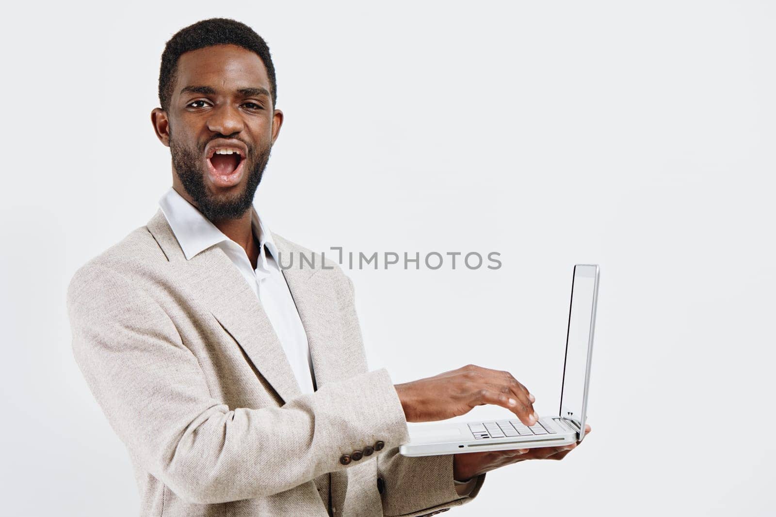Confident smiling man with dark skin, short curly hair, dressed in a beige blazer and white shirt, holding a laptop and looking friendly, isolated on a plain white background, studio shot, conveying tech and professional success.