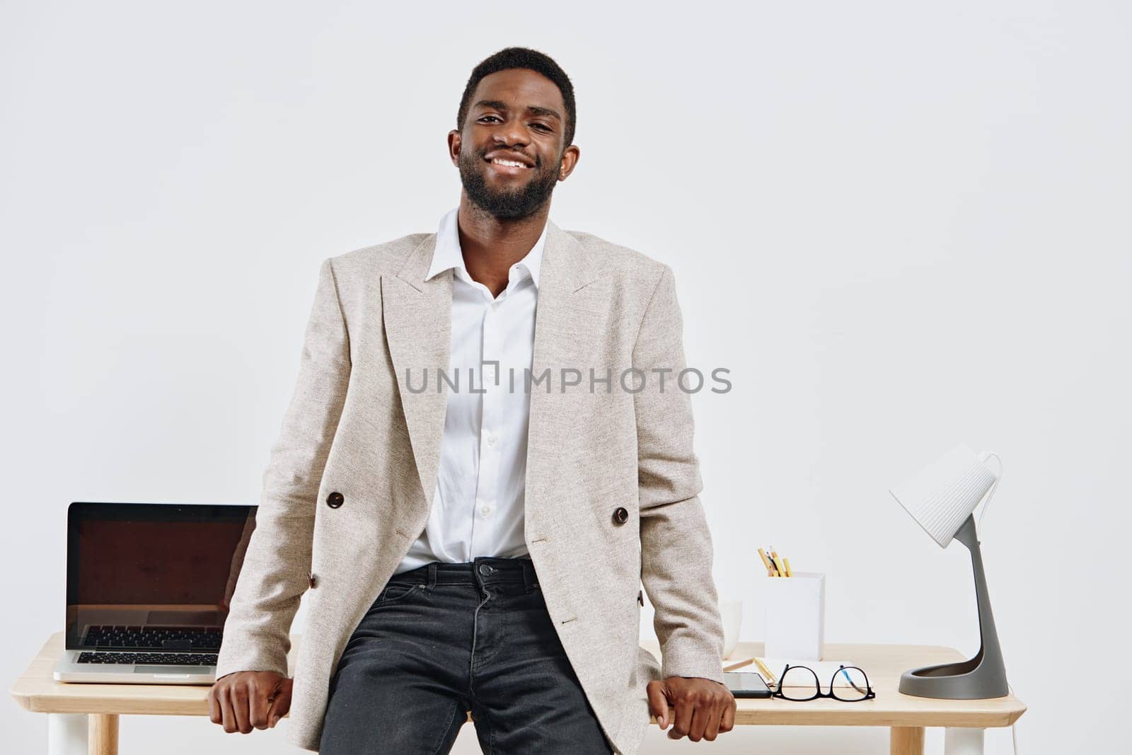 Smiling man in smart casual attire standing in a bright modern office with minimalistic decor and a laptop on the desk, creating a professional and approachable atmosphere. Concept: workplace positivity.