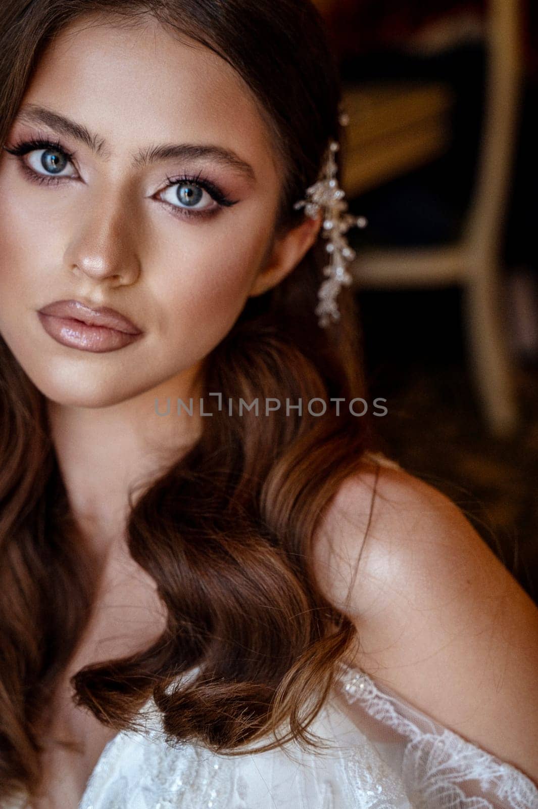 close-up, portrait of a young brunette bride in a white dress with a corset. Long hair is styled in a wave, white decoration of small pearls in her hair on the side. wedding makeup and hairstyle.