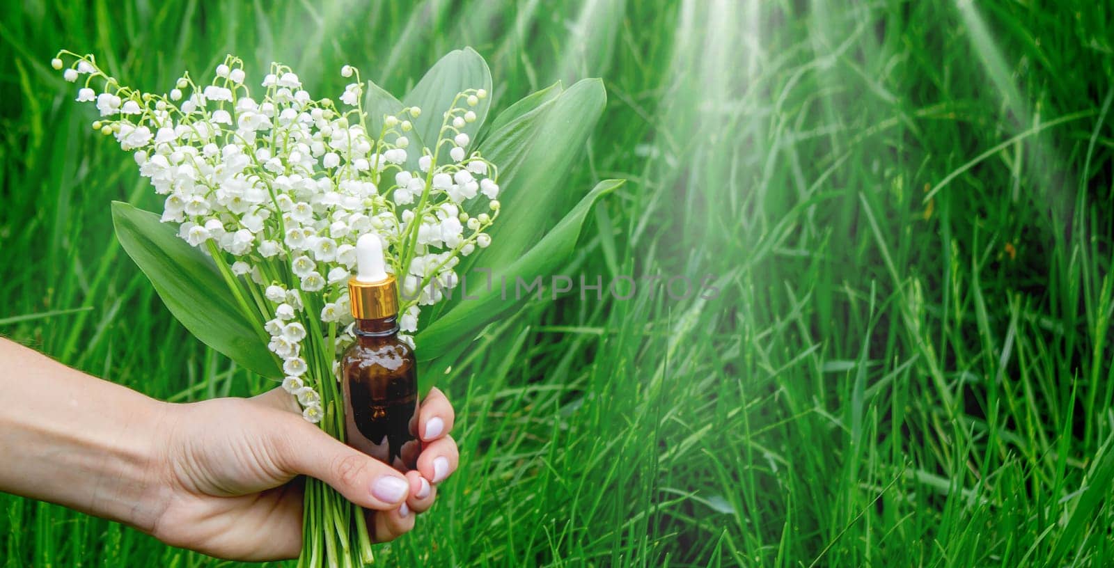 Glass bottle of lily of the valley essential oil with fresh flowers