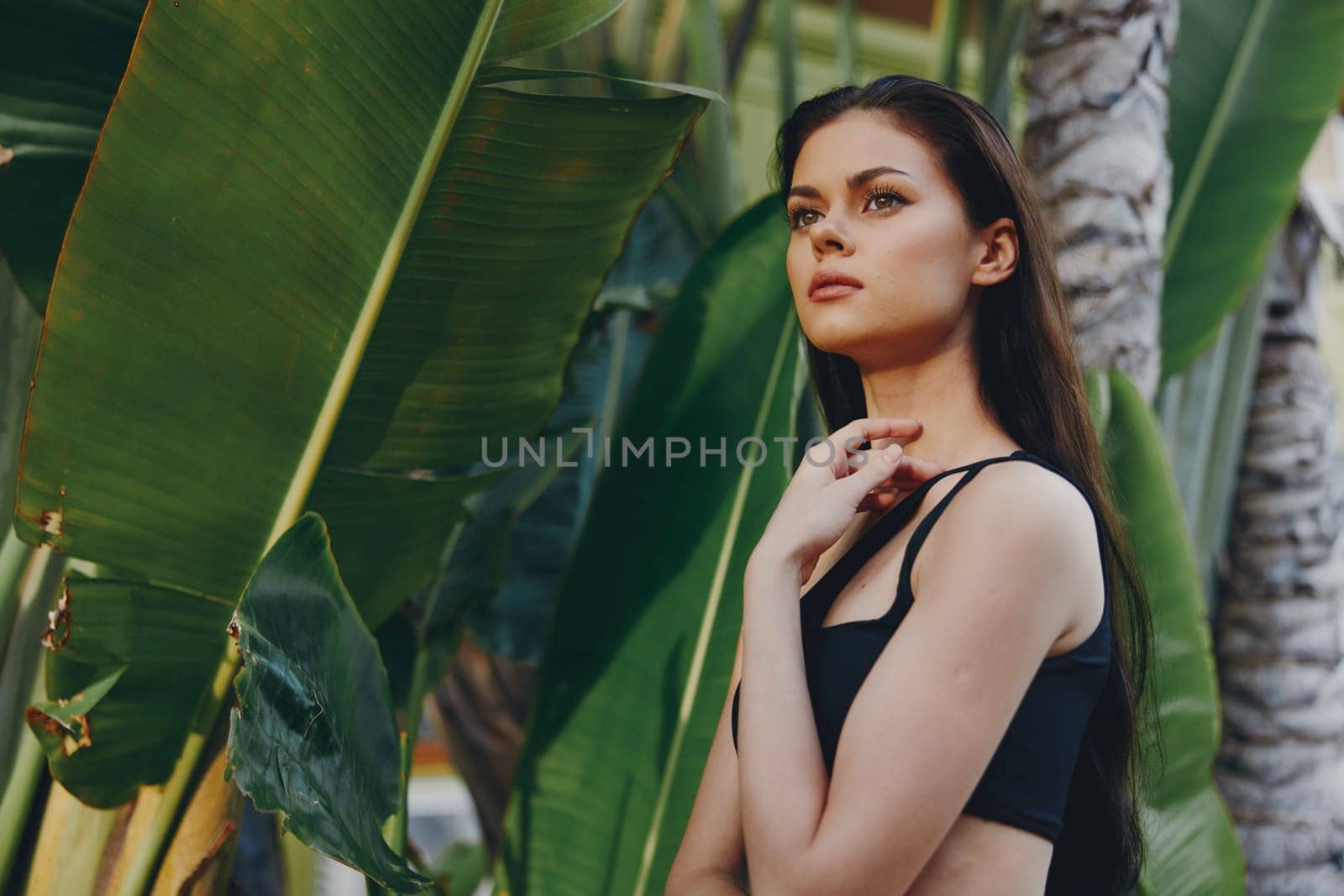 Confident woman in black bra top posing with hands on hips in front of tropical palm trees