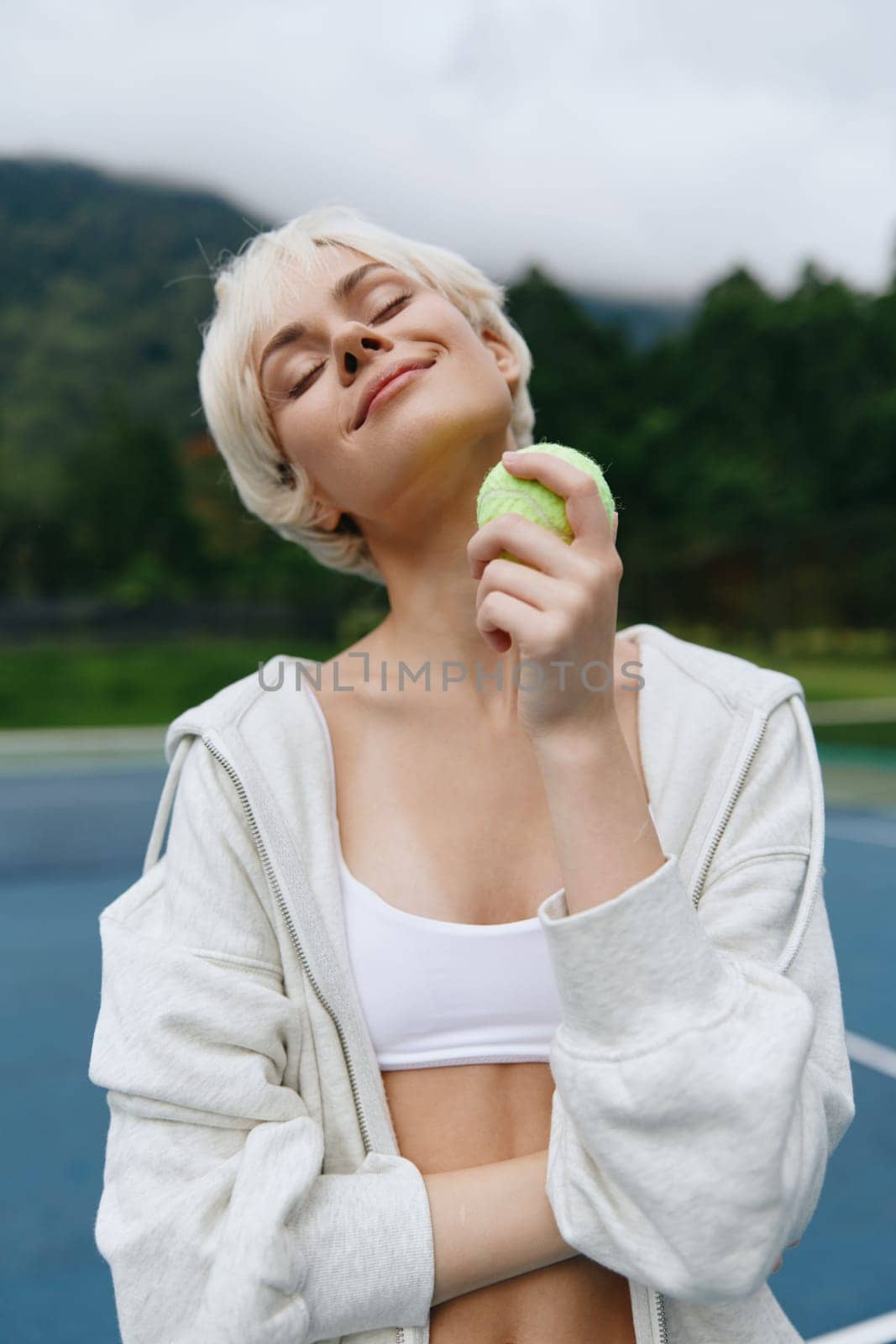 Smiling young woman holding apple, representing healthy lifestyle and fitness, dressed in sporty apparel on outdoor tennis court, conveying joy and vitality