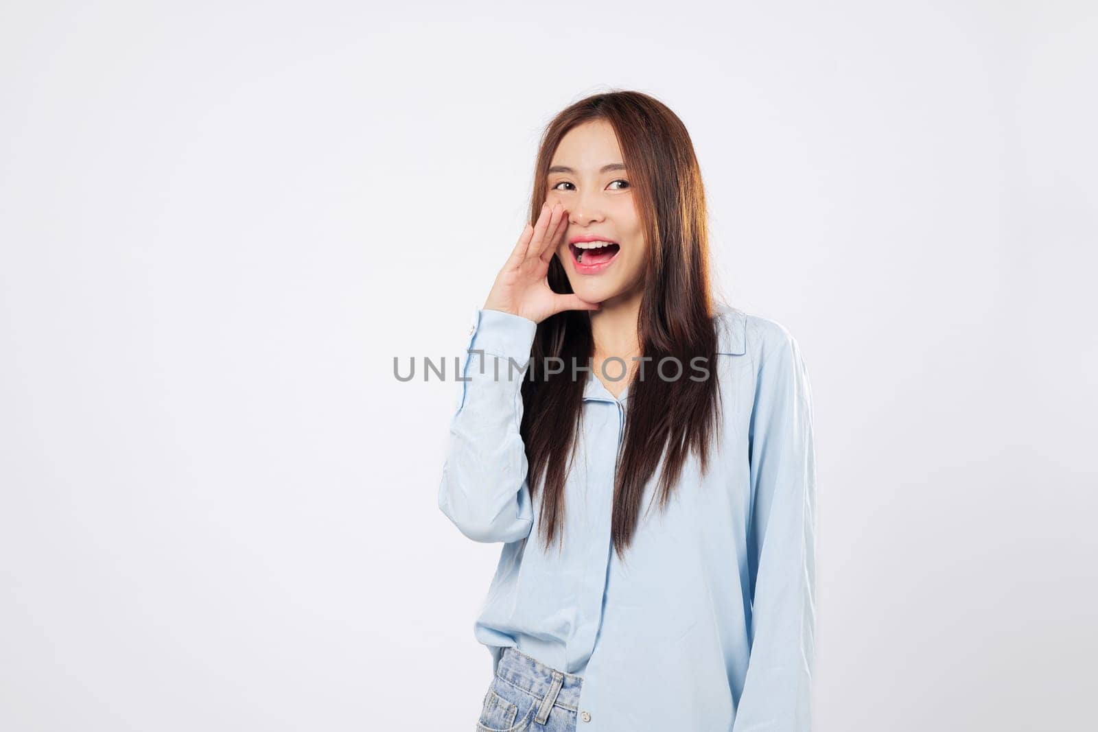 Shouting woman places hands on mouth while another woman makes a loud announcement, eyes wide with joy, expressing surprise and excitement isolated on a clean white background.