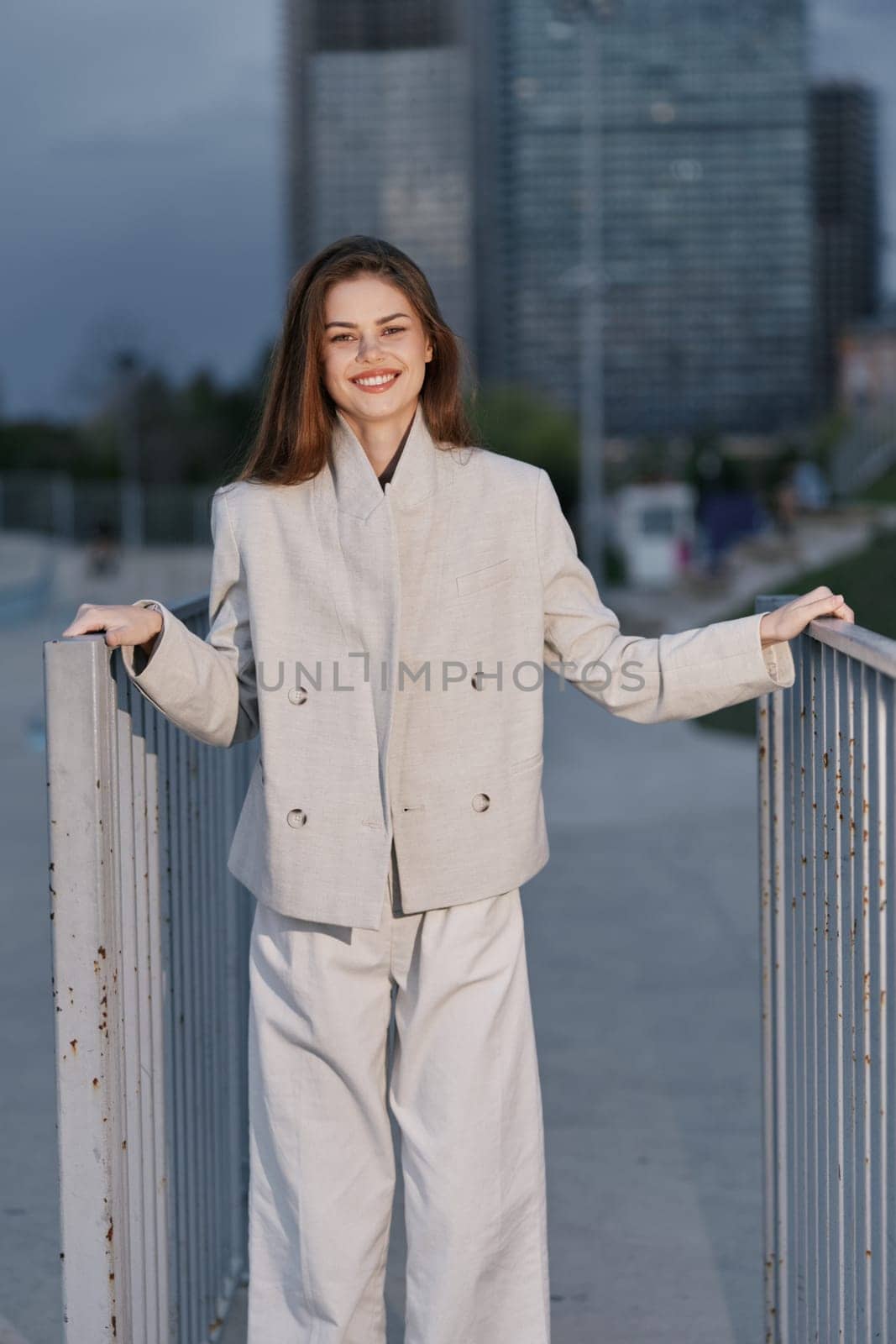 confident woman in beige business suit smiling outdoors with modern cityscape in background, natural light, and casual professional style.