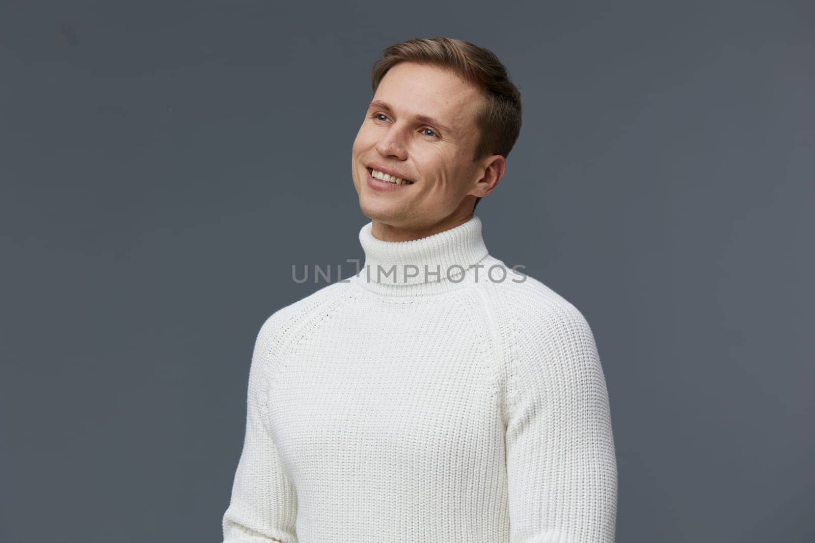 Portrait of a smiling man dressed in a white turtleneck sweater against a plain gray backdrop, showcasing a cheerful and relaxed demeanor, suitable for fashion, lifestyle, and portrait concepts.