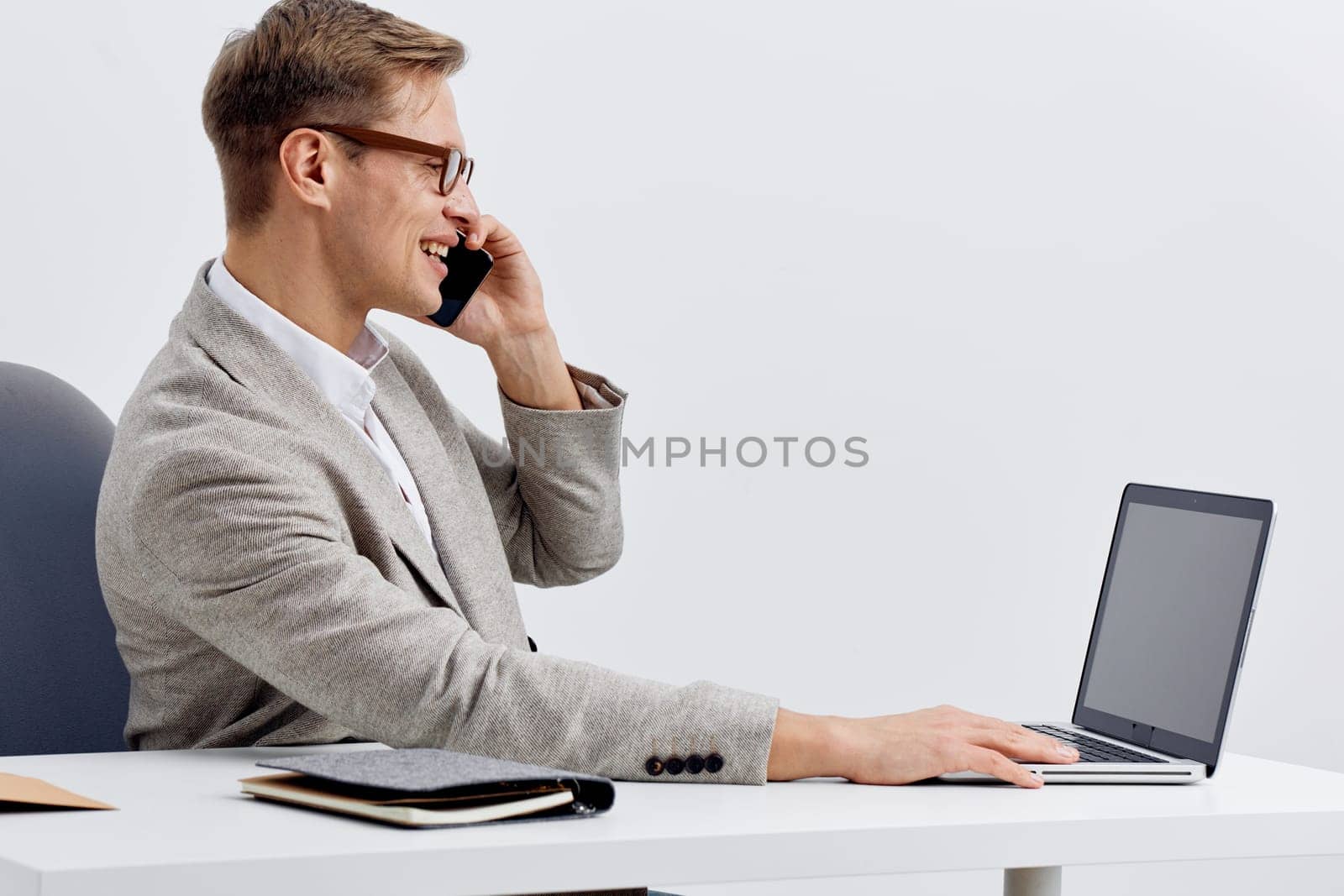 smiling man working with laptop and talking on mobile phone in modern office environment focused on smart home technology and digital nomad lifestyle with casual gray blazer and eyeglasses. Concept: smart home automation