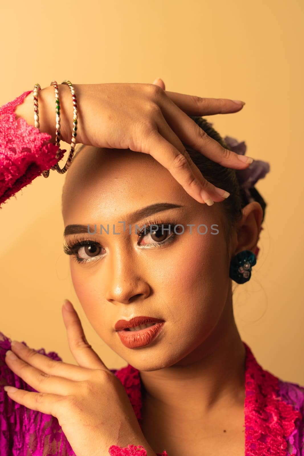 beautiful Balinese woman wearing makeup in a pink dress while posing with exotic hands inside the studio
