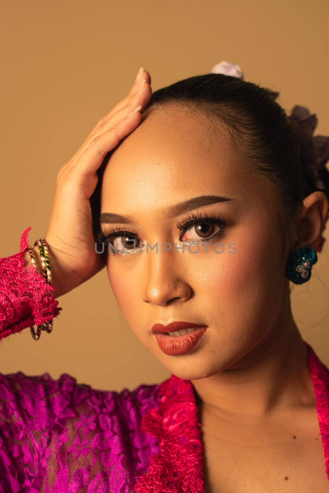 beautiful Balinese woman wearing makeup in a pink dress while posing with exotic hands inside the studio