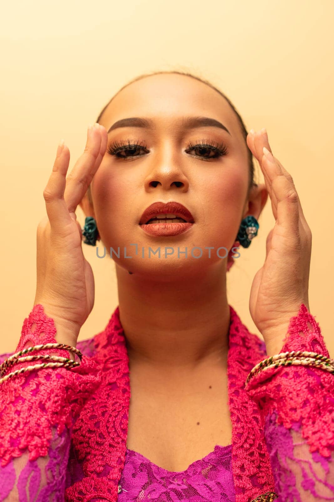 beautiful Balinese woman wearing makeup in a pink dress while posing with exotic hands inside the studio