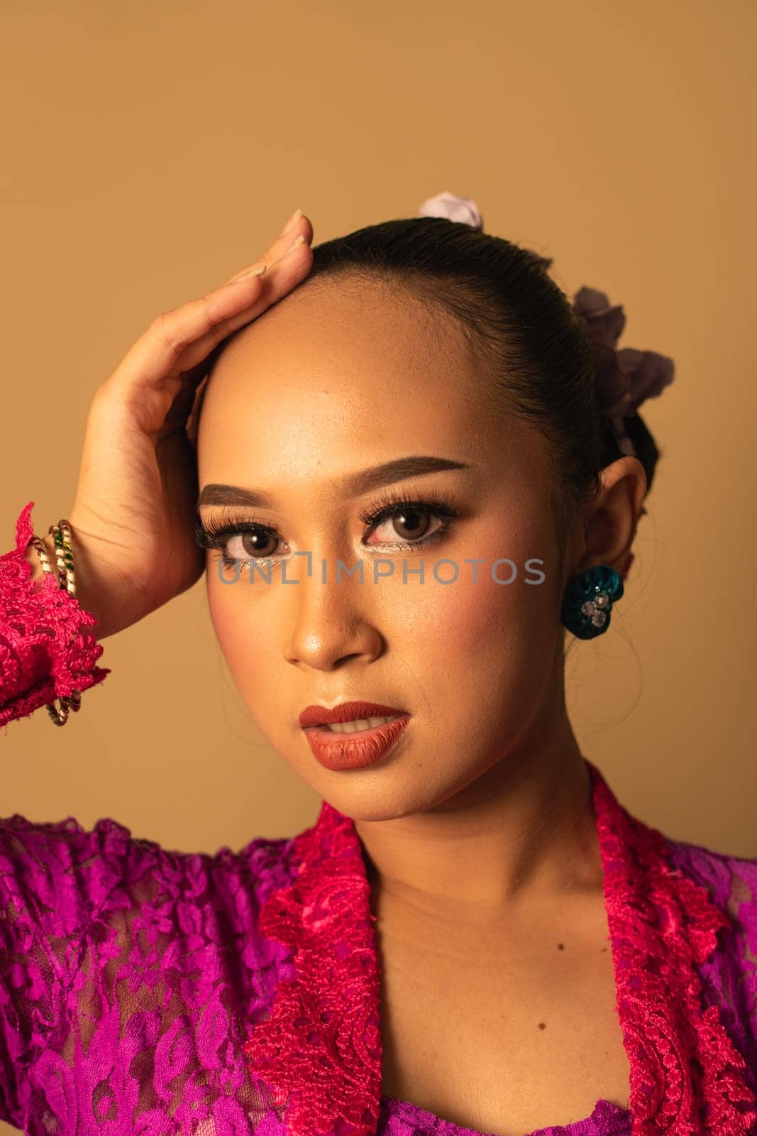 beautiful Balinese woman wearing makeup in a pink dress while posing with exotic hands inside the studio
