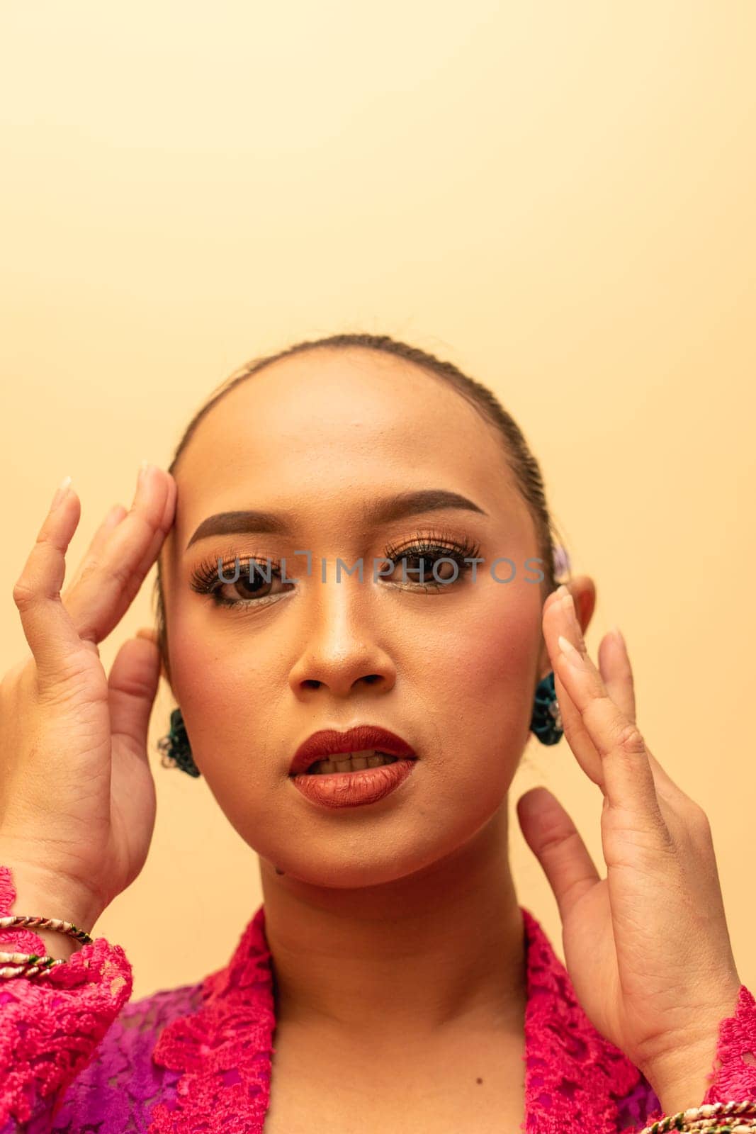 beautiful Balinese woman wearing makeup in a pink dress while posing with exotic hands inside the studio