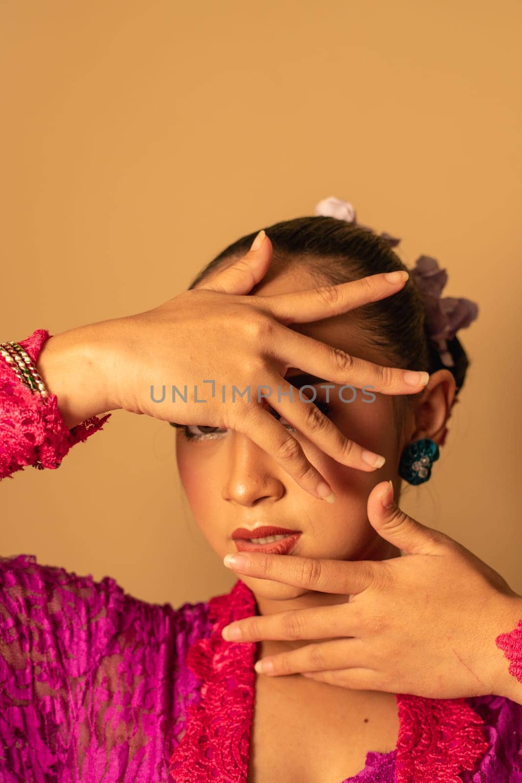 Portrait of Balinese woman with pink dress pose with hands on the face inside the room