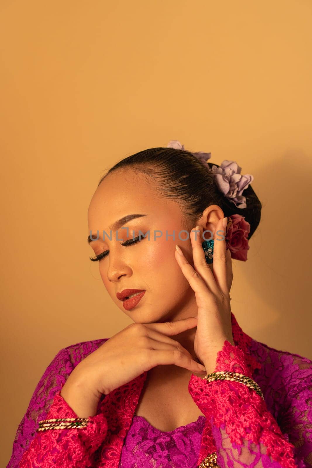 Portrait of Balinese woman with pink dress pose with hands on the face inside the room