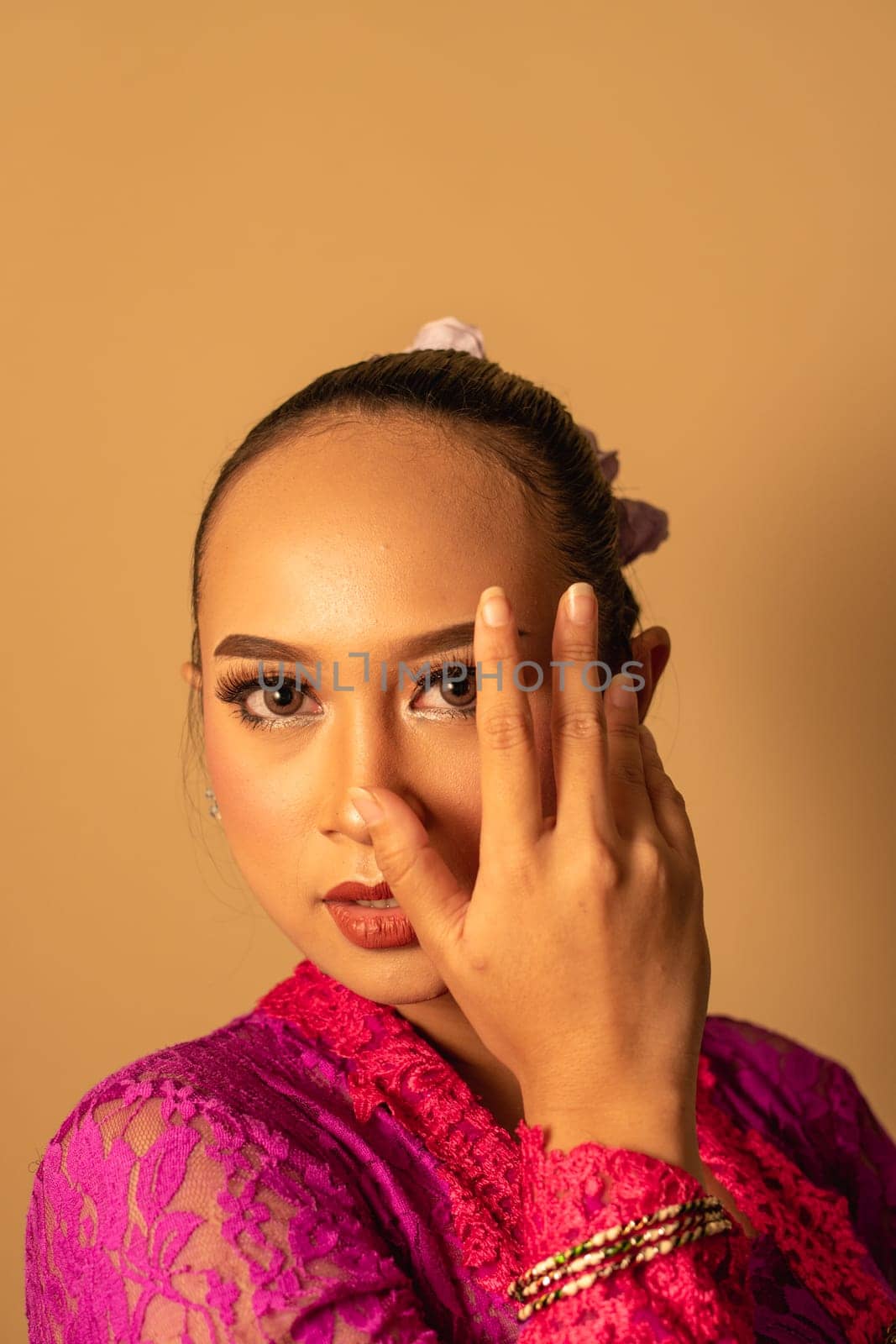 Portrait of Balinese woman with pink dress pose with hands on the face inside the room
