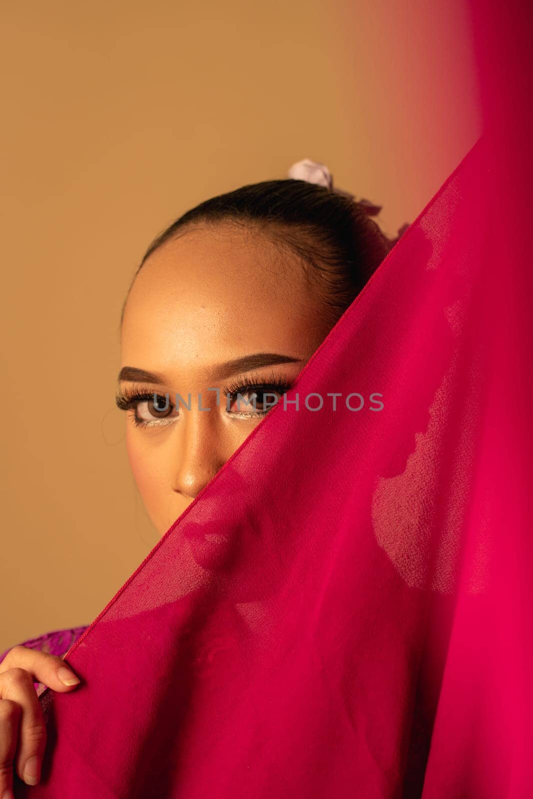 A beautiful Balinese woman covered her makeup face with red fabric from the dress inside the studio