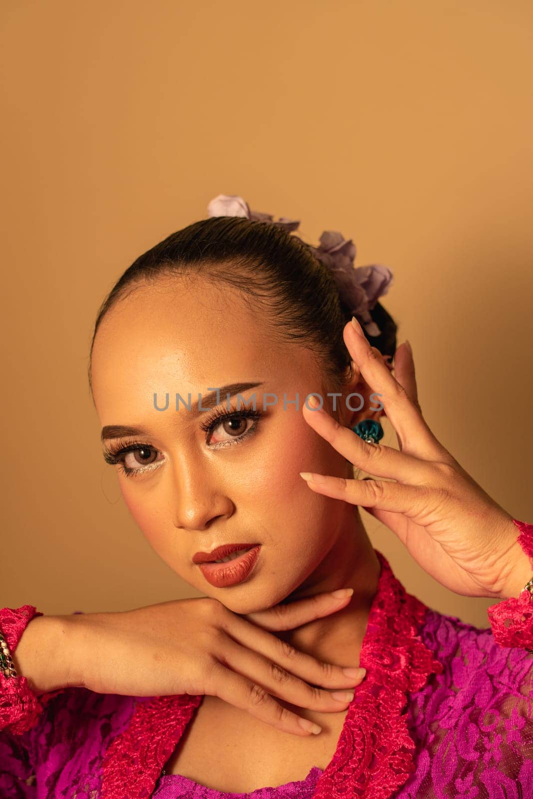 Portrait of Balinese woman with pink dress pose with hands on the face inside the room