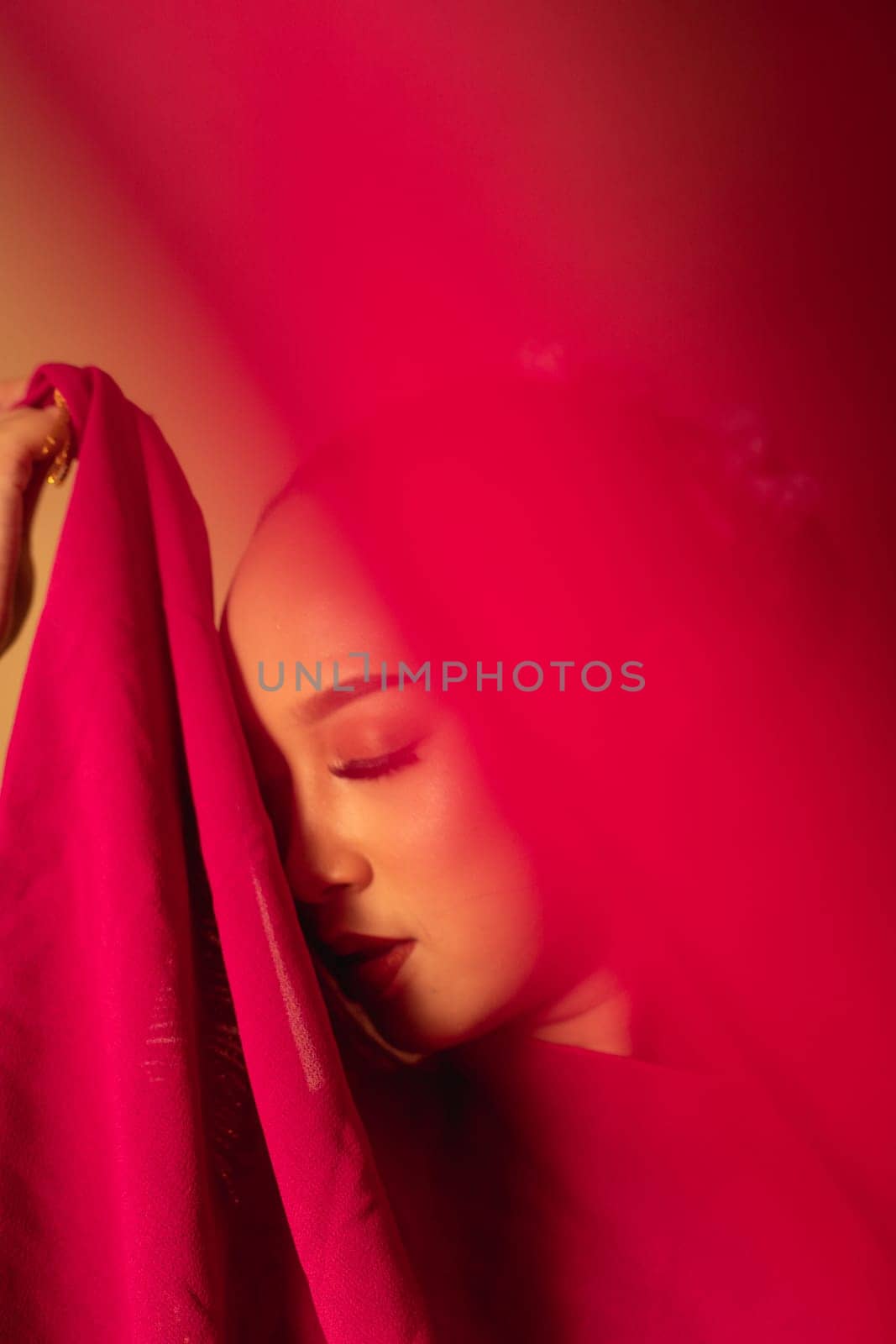 A beautiful Balinese woman covered her makeup face with red fabric from the dress inside the studio