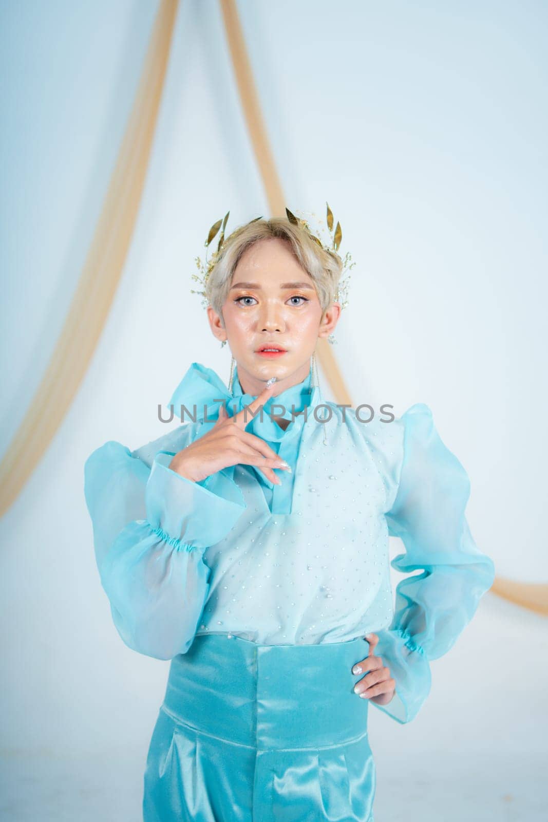 an elegant woman with blonde hair wearing a golden crown and a blue dress in a white room