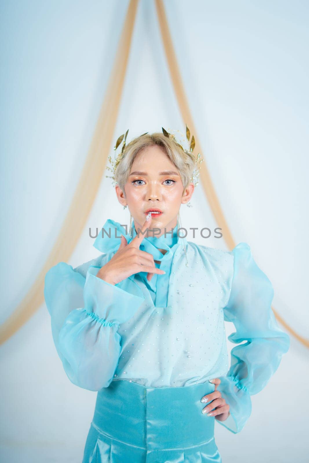 an elegant woman with blonde hair wearing a golden crown and a blue dress in a white room