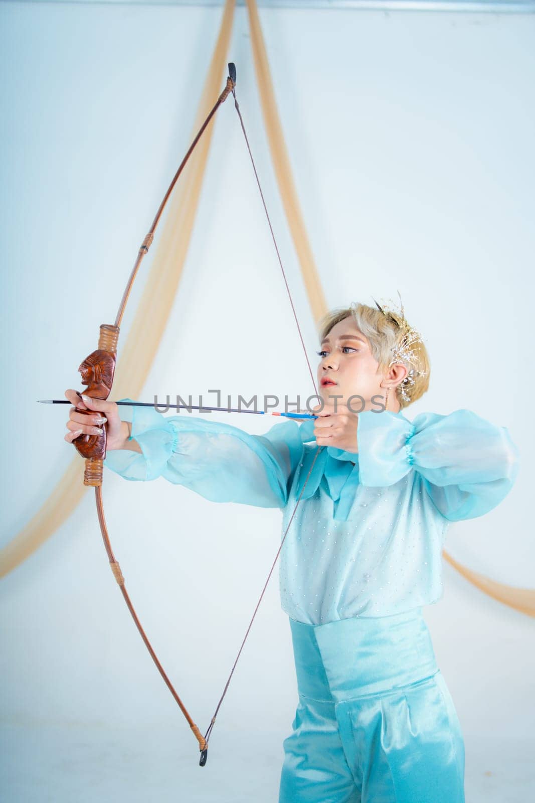 an Asian woman with blonde hair holding an arrow while wearing a blue dress in a white room
