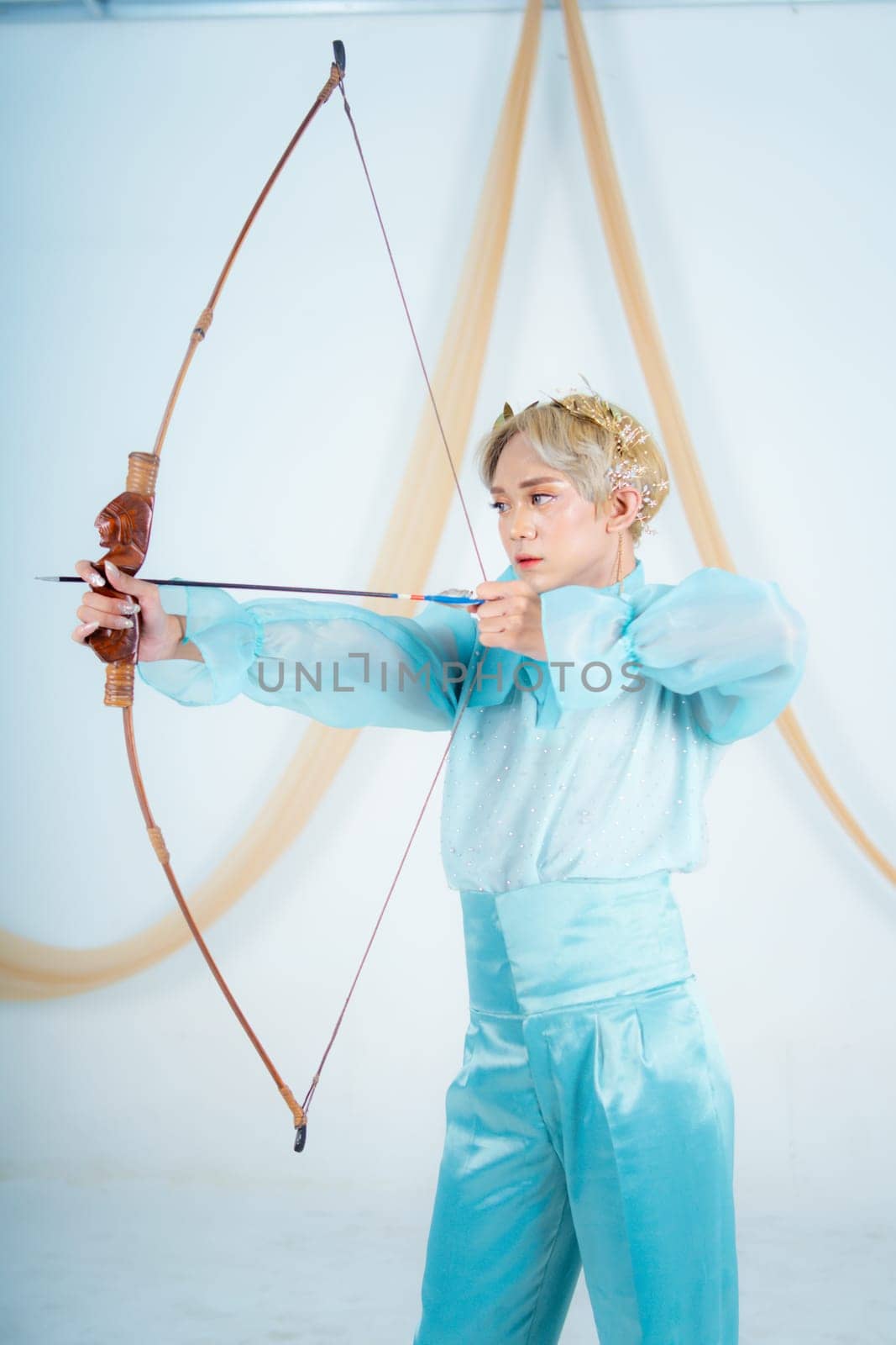an Asian woman with blonde hair holding an arrow while wearing a blue dress in a white room