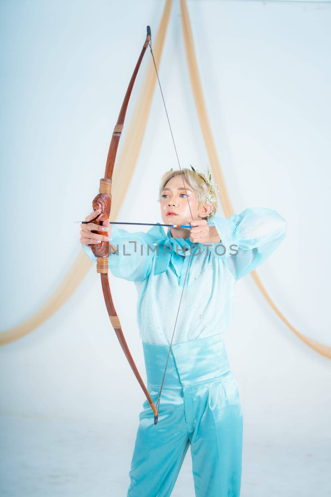 an Asian woman with blonde hair holding an arrow while wearing a blue dress in a white room