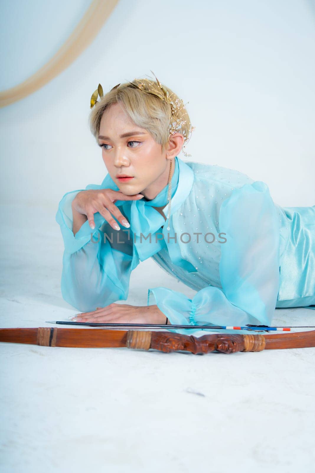 a princess in a blue dress posing on the floor with a bow in a white room