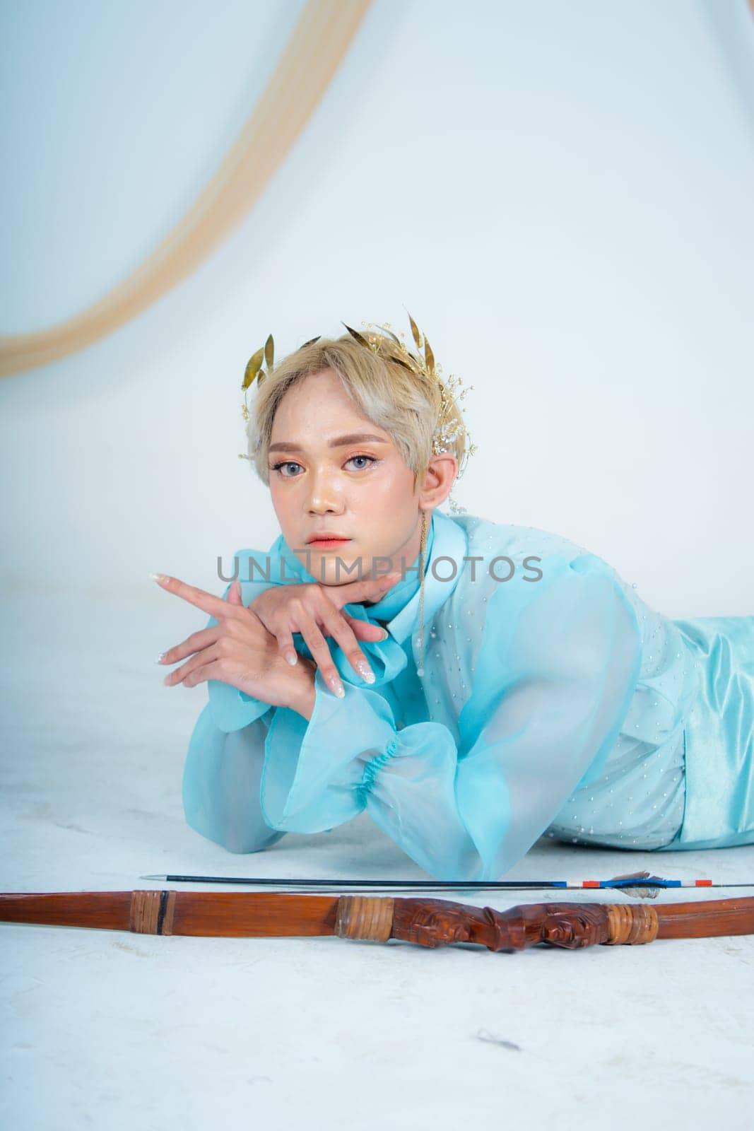 a princess in a blue dress posing on the floor with a bow in a white room