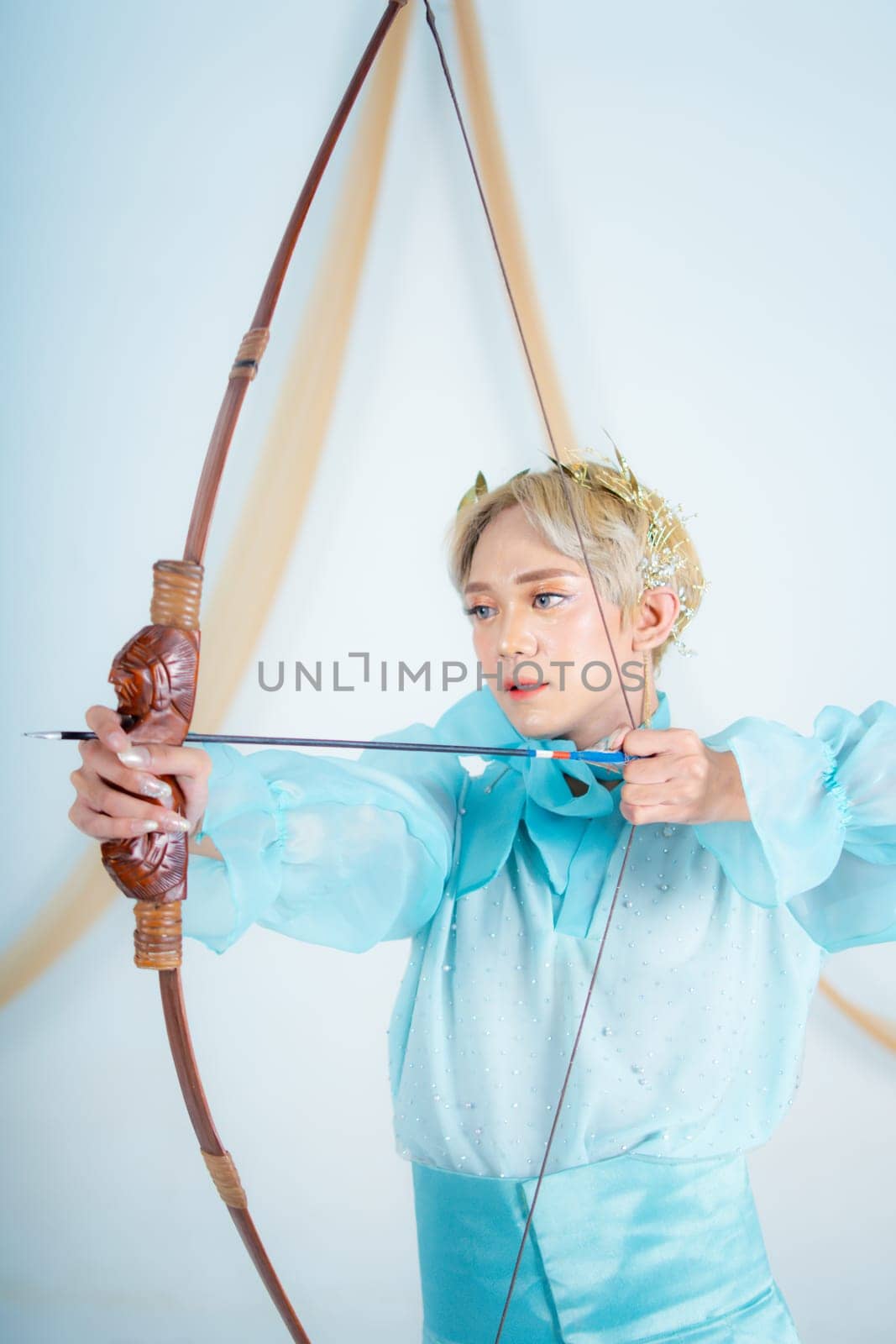 an Asian woman with blonde hair holding an arrow while wearing a blue dress in a white room