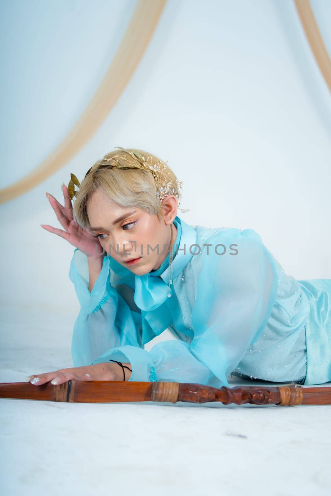 a princess in a blue dress posing on the floor with a bow in a white room